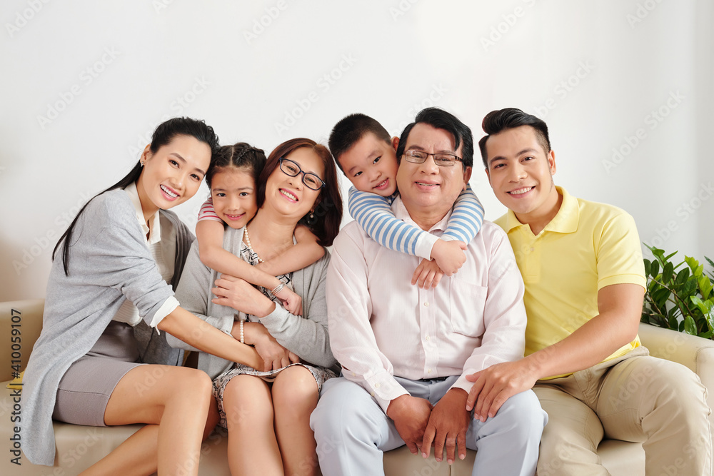 Cheerful Vietnamese children, parents and grandparents sitting on sofa in living room, hugging and looking at camera Cheerful Vietnamese children, parents and grandparents sitting on sofa in living room, hugging and looking at camera