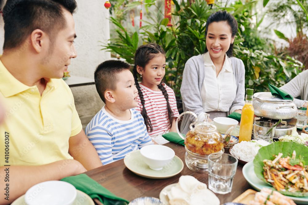 Cute little boy reciting poem for family when sitting at big dinner table outdoors Cute little boy reciting poem for family when sitting at big dinner table outdoors