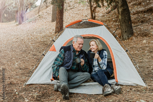 Happy old couple having coffee by the tent in the forest