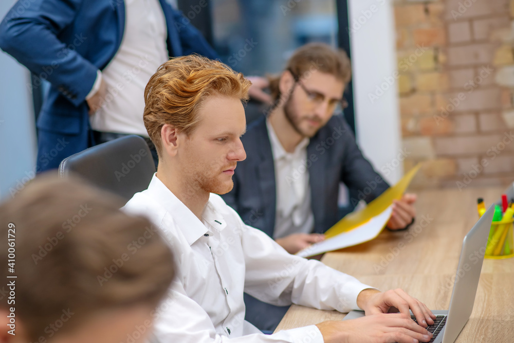 Obraz premium Redhaired man working at laptop and colleague managers