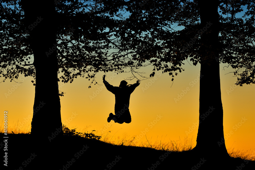 Silhouette of woman jumping under trees at sunset