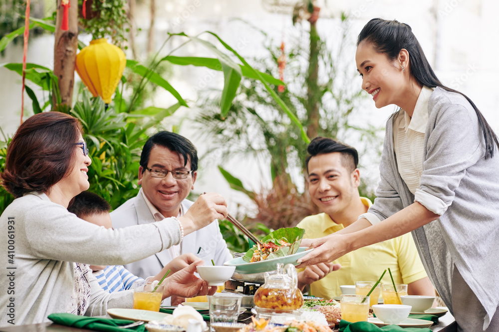 Naklejka premium Young beautiful Asian woman offering tasty salad to guests at family dinner