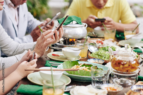 Cropped image of family members using social media on smartphones when having family dinner