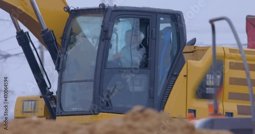 In winter, at a construction site, excavator remove a layer of earth to build the foundation of the future structure and load it into the bodies of dump truck. Operator work in the cab close-up 