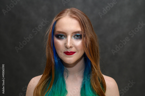 Photo of a happy woman. Portrait of a beautiful caucasian girl with dyed hair and excellent makeup on a gray background.