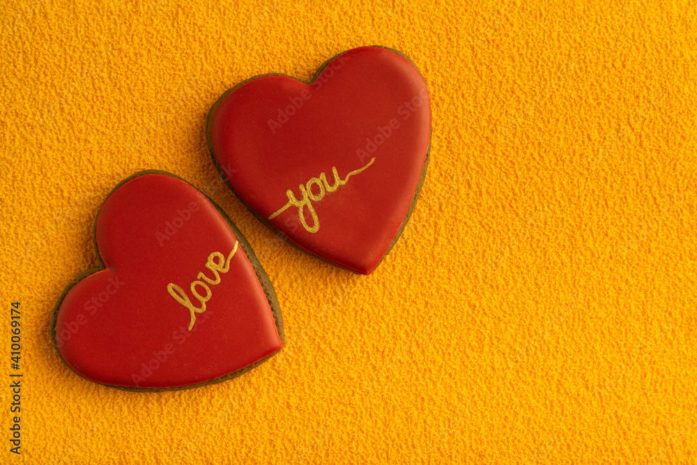 Obraz premium Two heart-shaped cookies with red sugar icing and inscription LOVE YOU, yellow background. Copy space