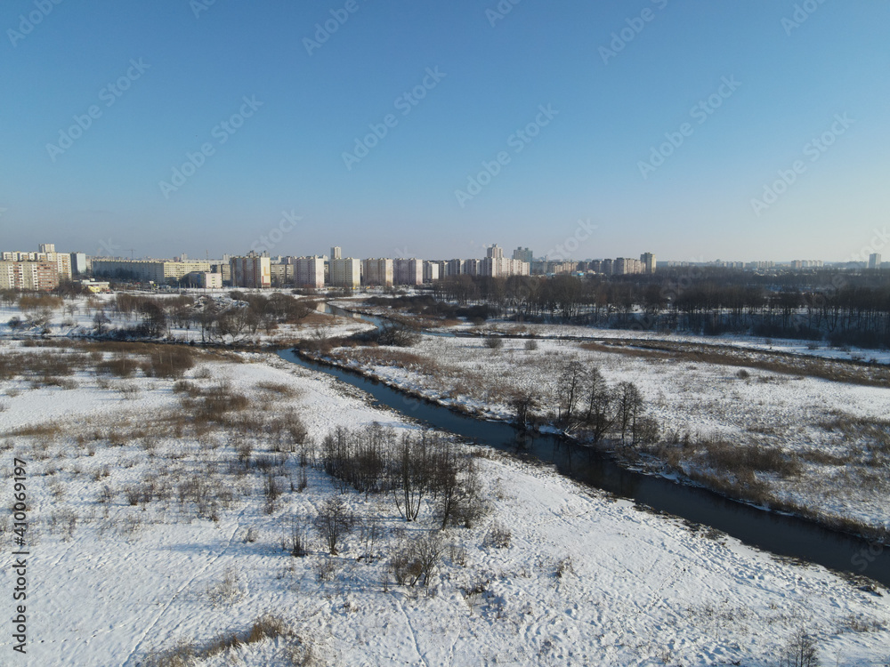 Urban winter landscape from above. Multi-storey buildings and trees in the city park are visible. River flows.