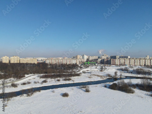 Urban winter landscape from above. Multi-storey buildings and trees in the city park are visible. River flows.