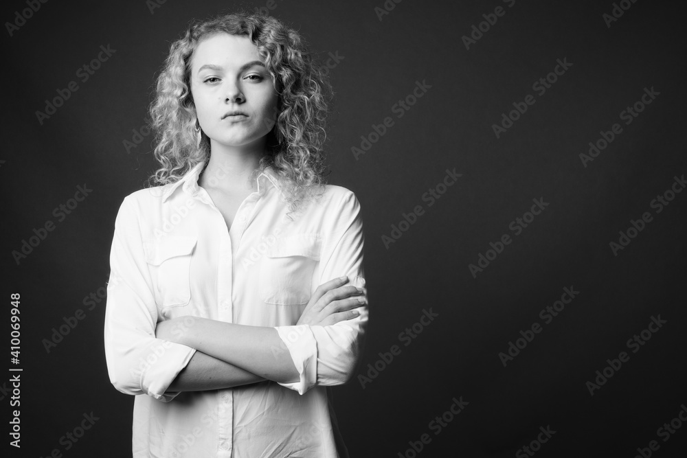 Young beautiful businesswoman with curly blond hair against gray background