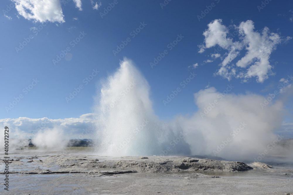 A small geyser at Yellowstone National Park erupting on a sunny day with a few clouds