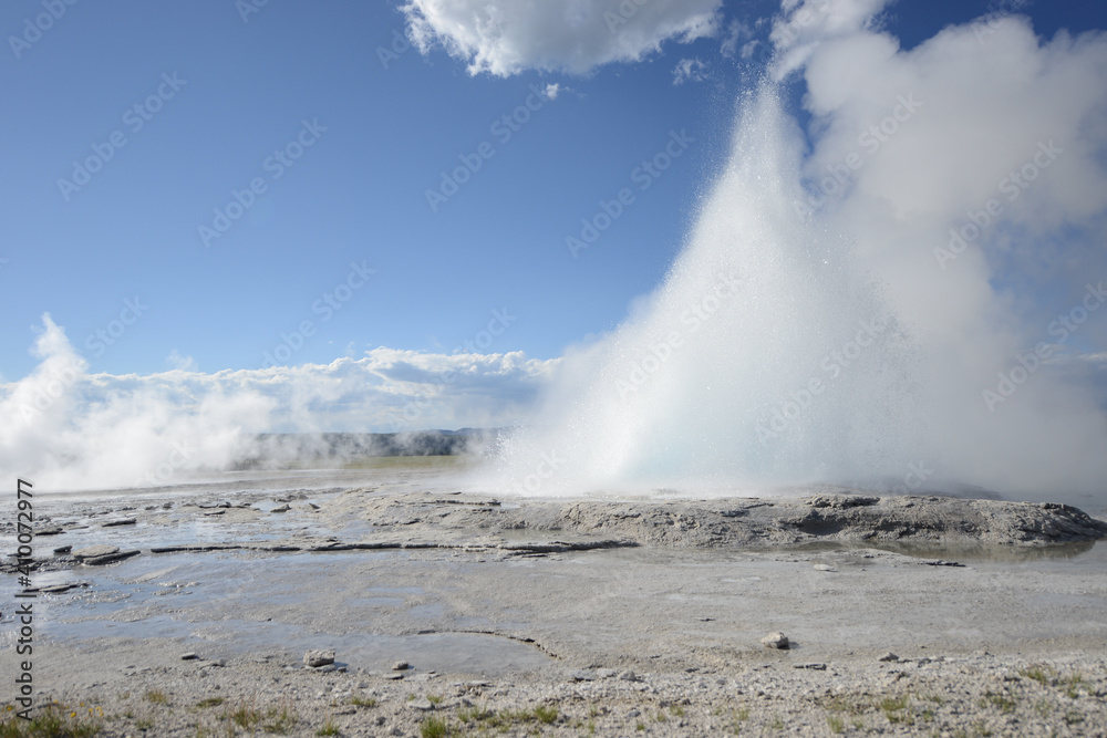 A small geyser at Yellowstone National Park erupting on a sunny day with a few clouds