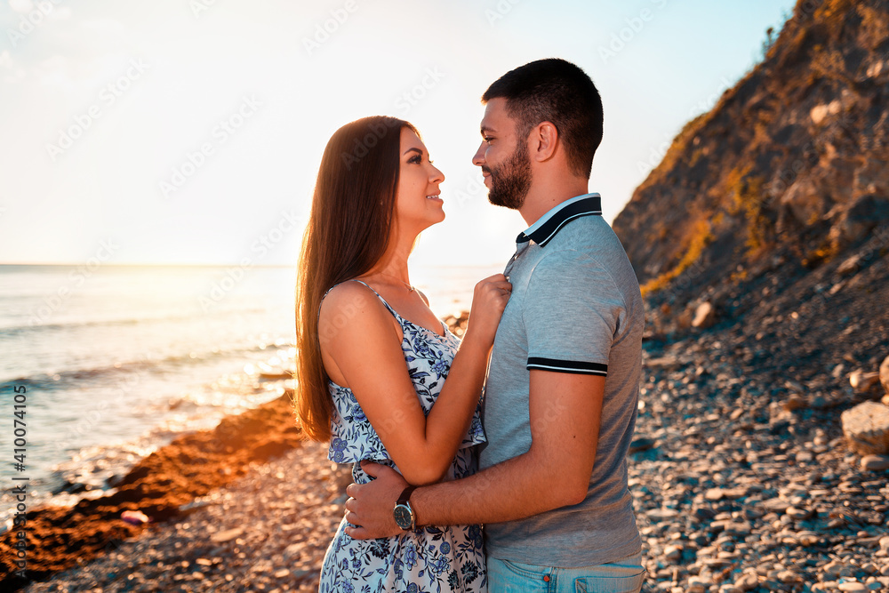 A young couple of lovers embrace and pose against the background of the beach, sea and sunset. Side view. The concept of Valentine's day
