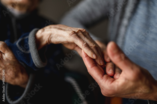 Unrecognizable young person holding hands of old woman. Elderly, care, family concept