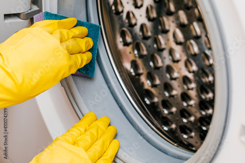 A man in yellow gloves cleans a dirty, moldy rubber seal on a washing machine. Mold, dirt, limescale in the washing machine. Periodic maintenance of household appliances