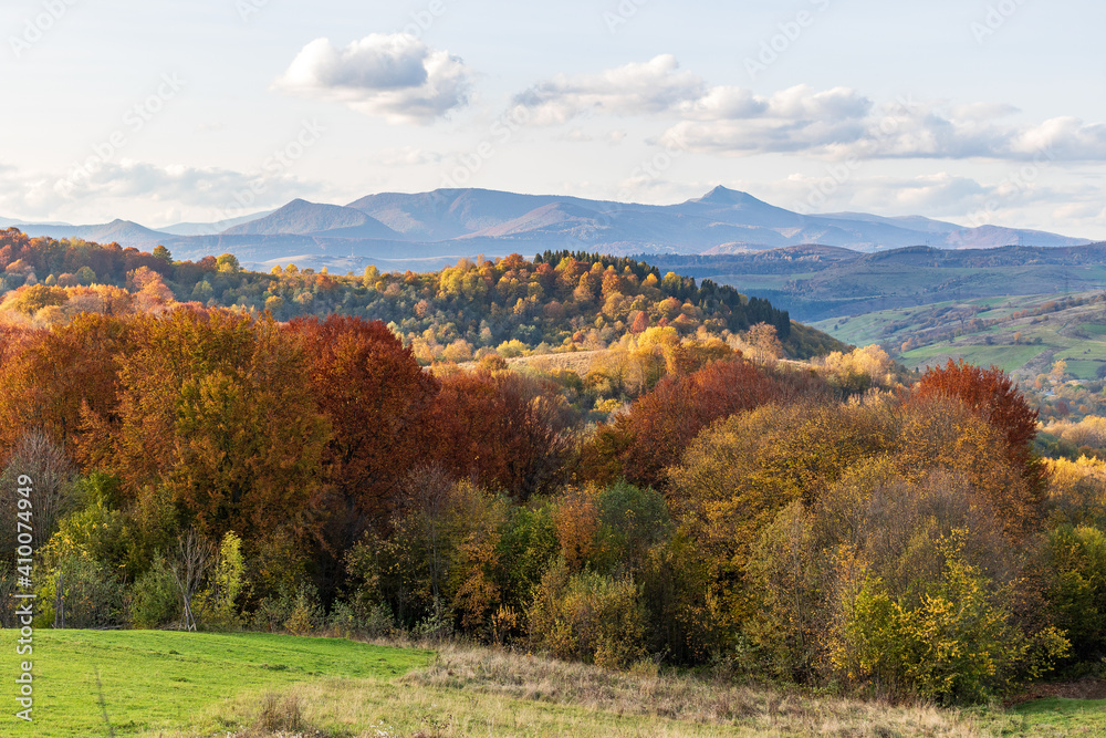 Autumn mountain landscape - yellowed and reddened autumn trees combined with green needles and blue skies. Colorful autumn landscape scene in the Ukrainian Carpathians. Panoramic view.