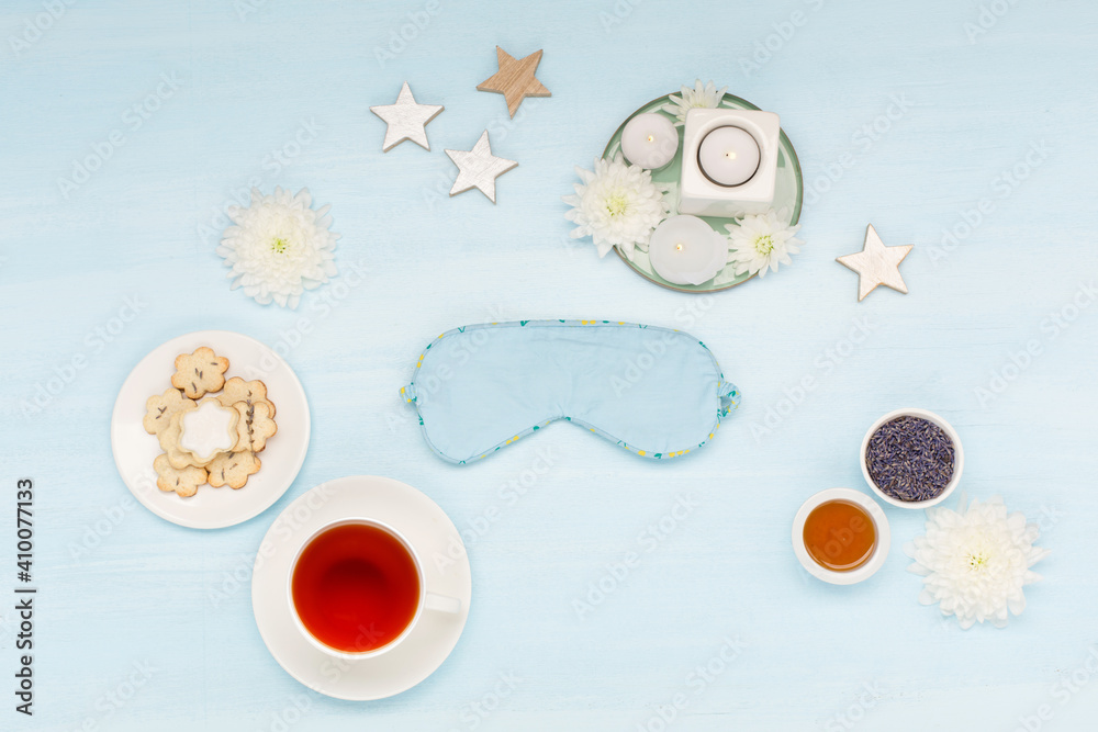 Cotton sleep mask, homemade cookies, cup of herbal tea, dry lavender flowers and candles on blue background. Top view, flat lay. Cotton sleep mask, homemade cookies, cup of herbal tea, dry lavender flowers and candles on blue background. Top view, flat lay.