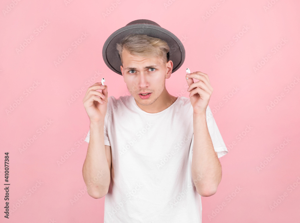 Portrait of a young man in a hat and white t-shirt, takes off wireless headphones and asks questions