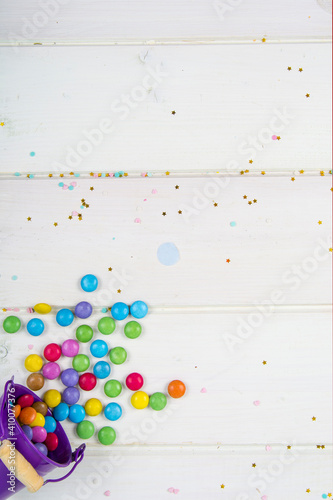 Colored candy bonbons scattered on white wooden board background