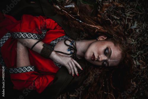 фотографія Red-haired woman in a red dress in a historical Celtic costume in the autumn for