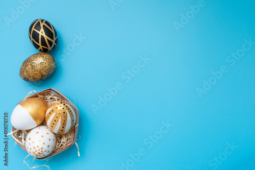Golden, black, white easter eggs on blue background. Geometry. Minimal easter concept. View from above. Easter card with copy space for text.