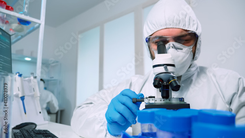 Laboratory scientist in ppe suit conducting experiment looking through a microscope in modern lab. Man working with various bacteria tissue, blood samples, concept of medical research for antibiotics