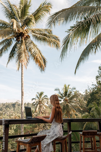Vertical photo woman freelancer working behind laptop sitting on the beach under a palm tree. Dream work.