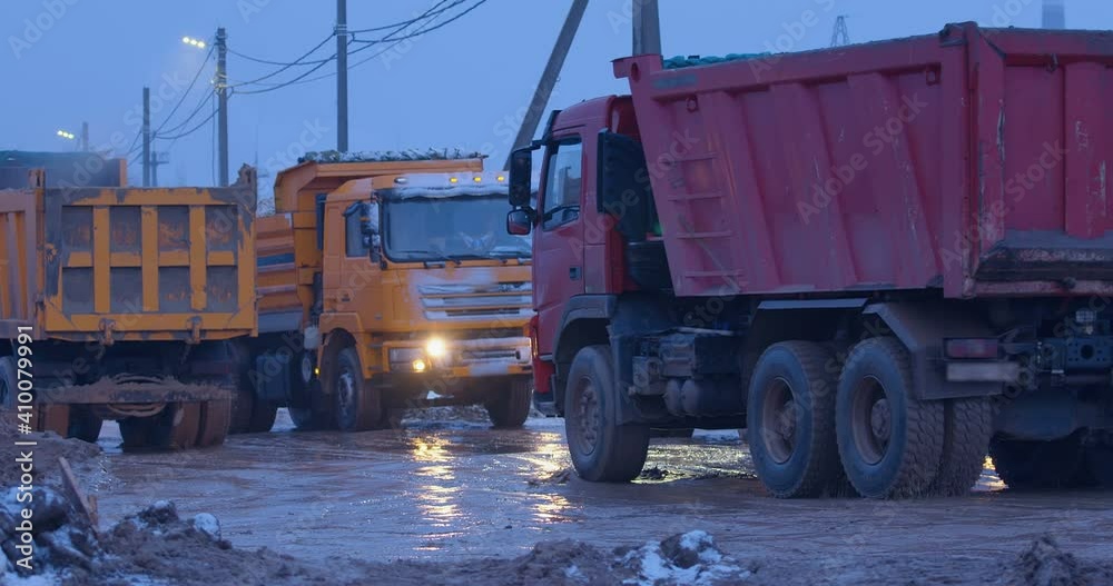 Excavation at a construction site, trucks with their headlights on are driving on a muddy road, some are carrying the land, some are waiting for their turn to load Excavation at a construction site, trucks with their headlights on are driving on a muddy road, some are carrying the land, some are waiting for their turn to load