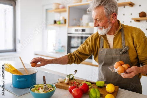 Happy retired senior man cooking in kitchen. Retirement, hobby people concept photo