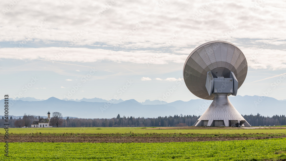 Backside view on a satellite dish of the Raisting Radome. In the distance the silhouette of mountains (alps) and a church.