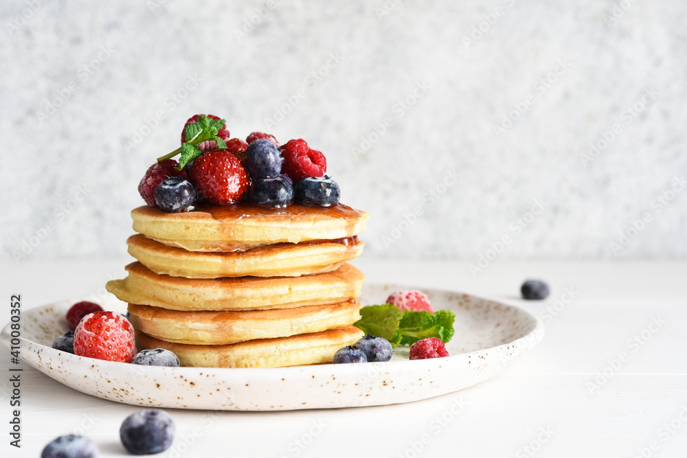 Pancakes with berries and maple syrup for breakfast on a light background. Pancakes with berries and maple syrup for breakfast on a light background.