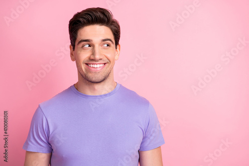 Portrait of attractive cheerful guy wear violet tshirt looking aside copy space isolated over pink pastel color background