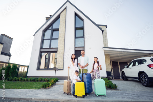 Photo portrait of smiling big full family with small kids outside house with luggage near car keeping bags ready to go for a trip