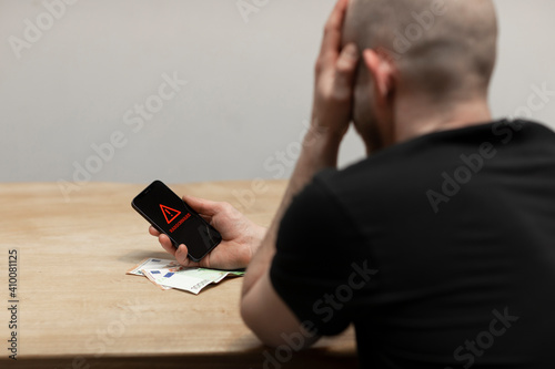 A ransomware text and warning sign popping up on a cell phone screen. A desperate man holding his hacked infected phone, ready to pay his blackmailer in cash. photo