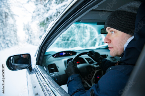 Man in warm winter clothes sitting in car. Snowy winter country road, car covered with ice, Beautiful forest under the snow. 