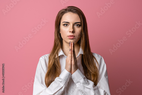 Attractive brunette girl prays for wellness of family, keeps palms pressed together in praying gesture, saying namaste