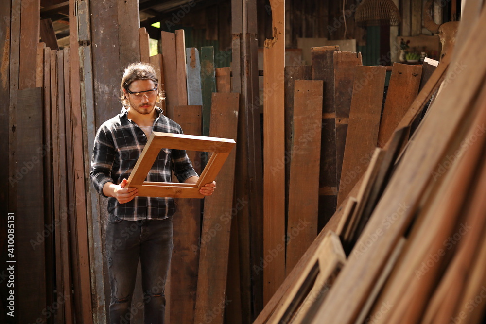 Young Caucasian carpenter man is making wooden frame in his own garage style workshop for hobby with copy space Young Caucasian carpenter man is making wooden frame in his own garage style workshop for hobby with copy space