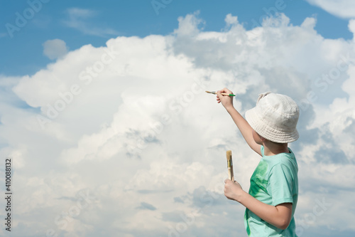 Young artist paints a beautiful sky and three-dimensional clouds with brushes in his hands