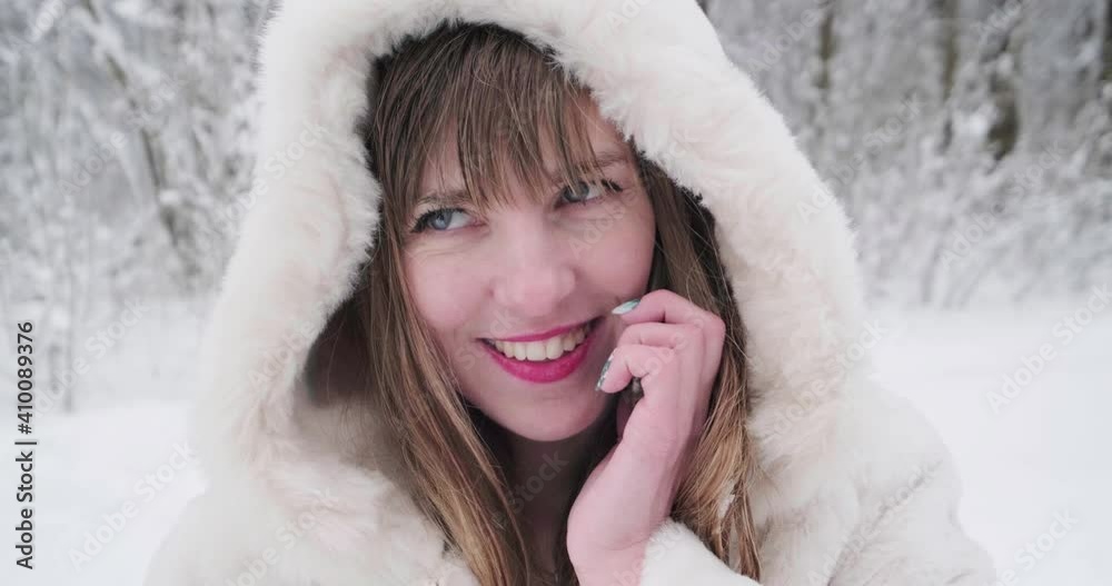 Close up portrait beautiful smiling confident young white woman pretty face in a white fur coat looking at camera and phone posing alone at snowy forest Close up portrait beautiful smiling confident young white woman pretty face in a white fur coat looking at camera and phone posing alone at snowy forest