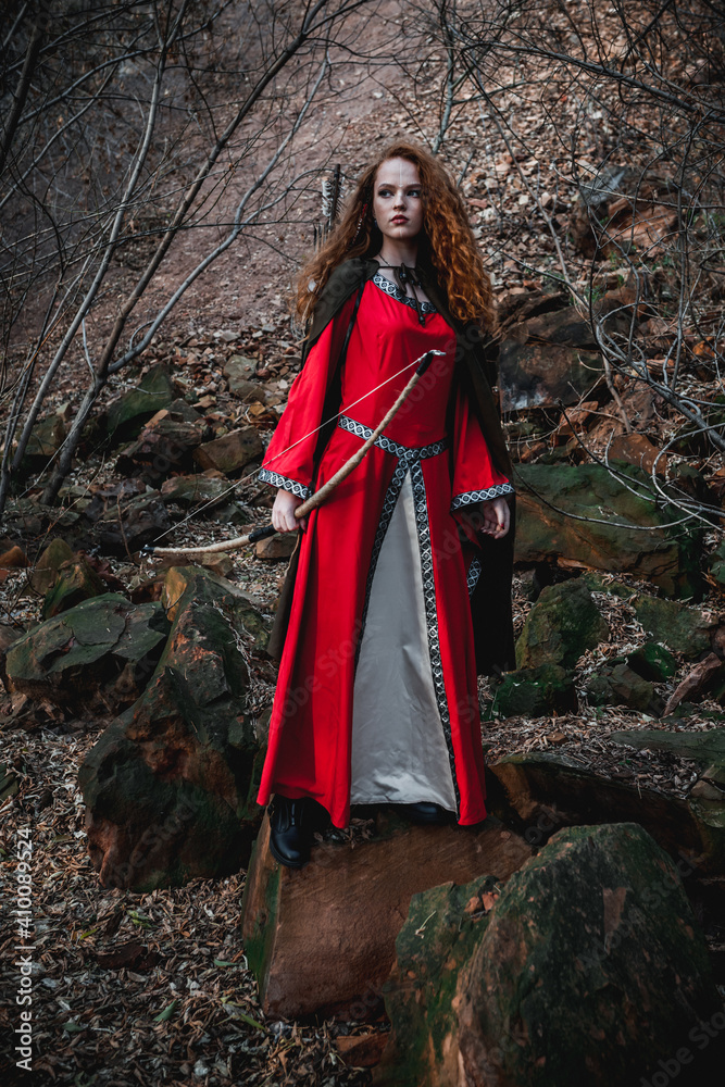 Red-haired woman in a red dress in a historical Celtic costume in the autumn forest Red-haired woman in a red dress in a historical Celtic costume in the autumn forest