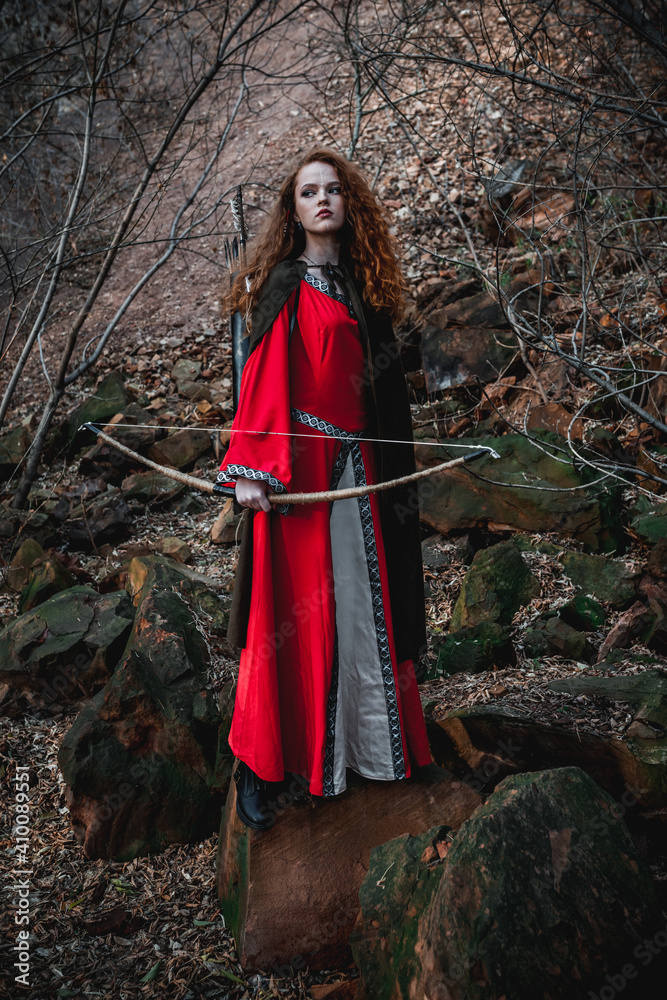 Red-haired woman in a red dress in a historical Celtic costume in the autumn forest Red-haired woman in a red dress in a historical Celtic costume in the autumn forest