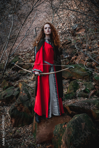 Red-haired woman in a red dress in a historical Celtic costume in the autumn forest