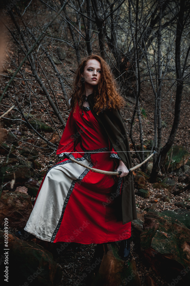 Red-haired woman in a red dress in a historical Celtic costume in the autumn forest Red-haired woman in a red dress in a historical Celtic costume in the autumn forest