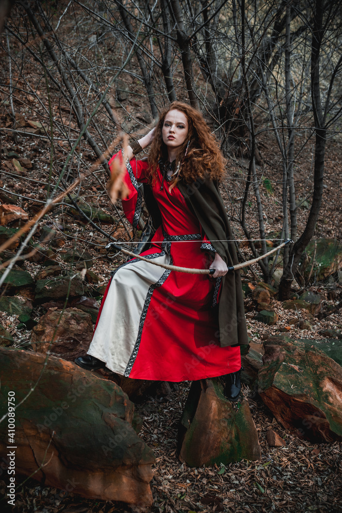 Red-haired woman in a red dress in a historical Celtic costume in the autumn forest Red-haired woman in a red dress in a historical Celtic costume in the autumn forest
