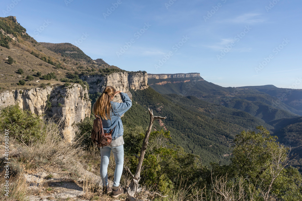 Fototapeta premium Young woman with jeans and backpack looking into the distance horizon with hand in head .Amazing mountains landscape with forest.Traveling on holidays, vacation lifestyle concept.