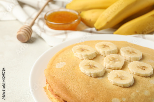 Concept of breakfast with plate of thin pancakes with banana, and jam on white textured background