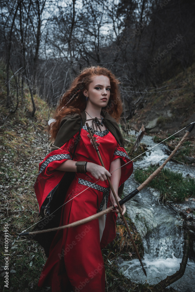 Red-haired woman in a red dress in a historical Celtic costume in the autumn forest