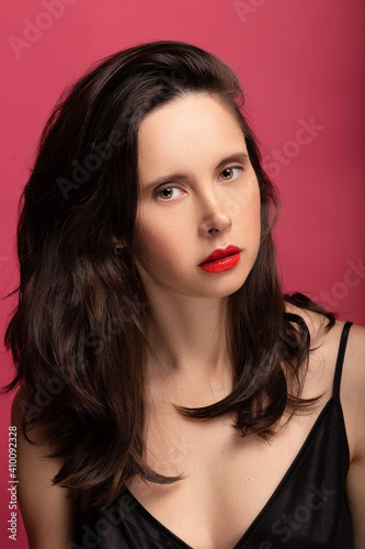 dark-haired girl on a pink background in a black t-shirt with red lipstick close-up