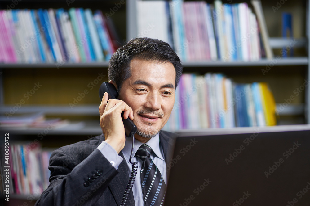 asian corporate executive working in office talking on phone