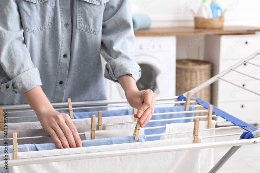 Woman hanging clean laundry on drying rack in bathroom, closeup Woman hanging clean laundry on drying rack in bathroom, closeup