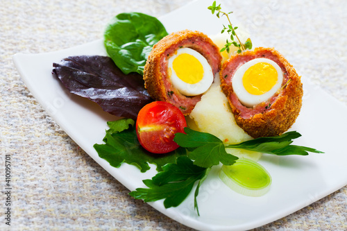 Delicious Scotch eggs with quail eggs served with mashed potato, onion, tomatoes and greens